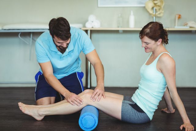 Physiotherapist performing leg therapy on a female patient using a foam roller in a clinic. Ideal for use in articles or advertisements related to physiotherapy, rehabilitation, physical therapy, healthcare services, sports injury recovery, and wellness programs.