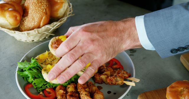 A middle-aged Caucasian businessman is reaching for food at a buffet, with copy space. His choice includes a variety of options such as skewered meats, salad, and bread rolls.