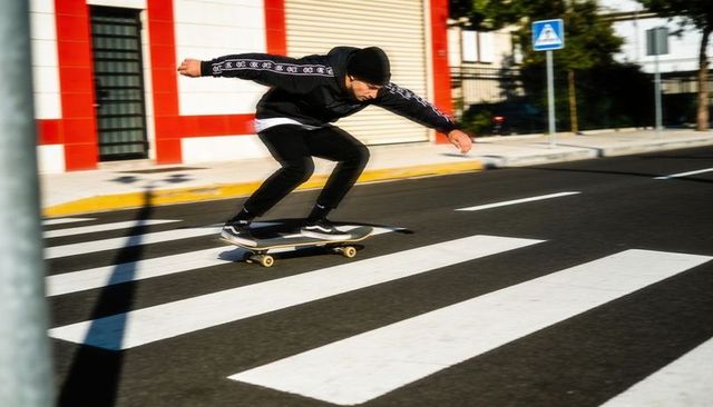 Skateboarder crouching low on crosswalk racing through urban sunlight