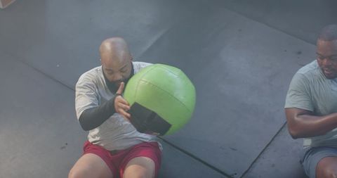 African men performing partner core workout passing green medicine ball in gym session