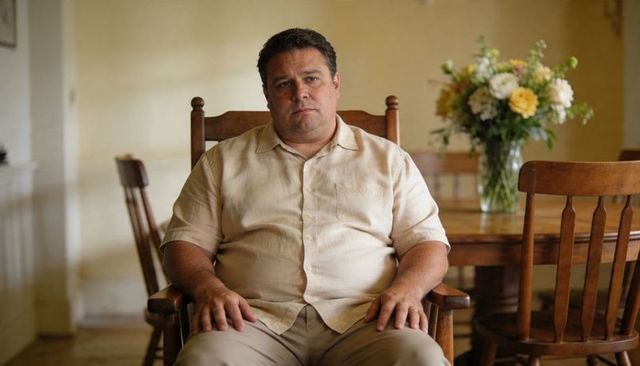 Middle-aged man sitting contemplating in wood armchair at cozy neutral dining interior