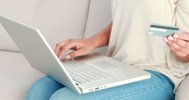 Female holding a credit card in one hand while using a laptop for online shopping or banking. Perfect for illustrating concepts related to e-commerce, financial transactions, digital banking, online security, and modern consumer behavior.