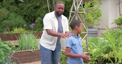 African-american father placing hand on son's shoulder in garden teaching care and growth