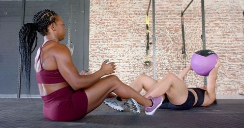 Female Athletes Performing Medicine Ball Sit-ups in Gym