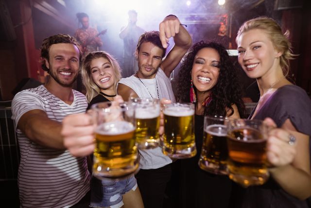 Portrait of happy young friends holding beer mugs together at nightclub