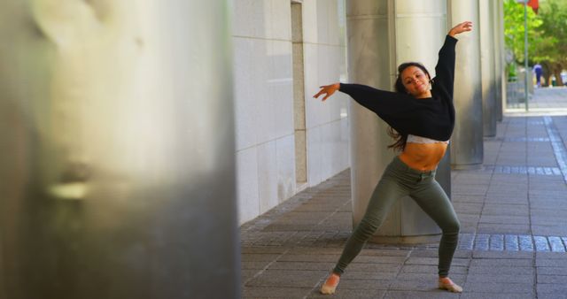 Young woman dancing outdoors against a cityscape background. The dancer uses contemporary dance movements, bringing urban elements to her routine. This can be used for promoting dance studios, urban dance events, fitness classes, or inspirational art and wellbeing campaigns.
