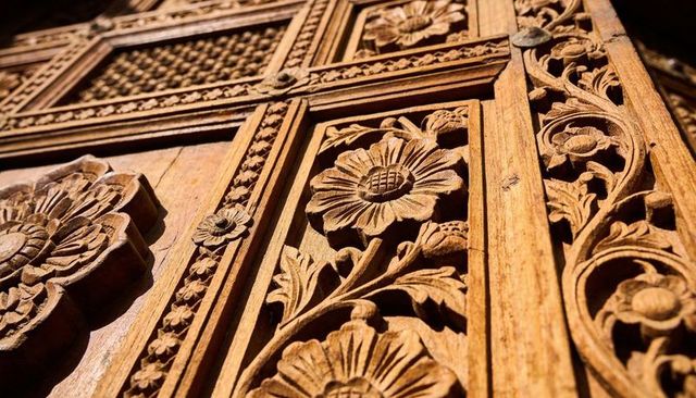 Ornate floral wood carving closeup featuring rosettes and vines on antique temple door