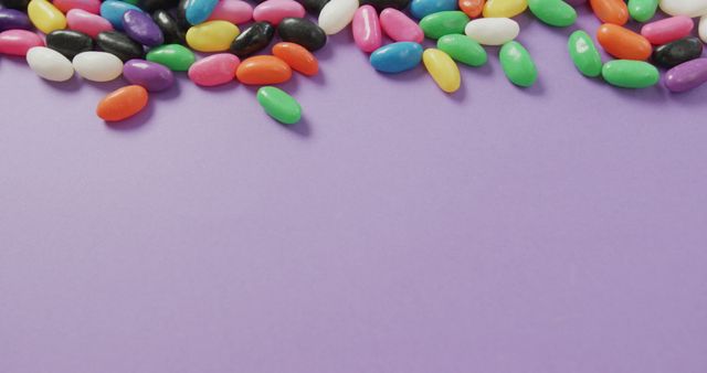 This vibrant photo displays an assortment of colorful jelly beans scattered on a purple background. It is perfect for use in advertising confectionery products, illustrating articles on sweet treats, or designing festive and fun marketing materials. The bright and diverse colors make it eye-catching, ideal for use in visual content that aims to appeal to candy lovers or highlight the joy of sweets.