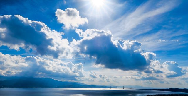 Bright sun over distant mountains with scenic bridge and fluffy clouds - Download Free Stock Photos Pikwizard.com