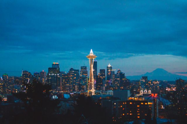 Image features iconic Seattle skyline with Space Needle illuminated at twilight. City lights create beautiful contrast against evening sky. Ideal for travel blogs, tourism websites, or promotional materials highlighting Seattle attractions and nightlife.