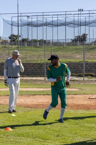 Senior coach signaling while player running during community baseball practice session