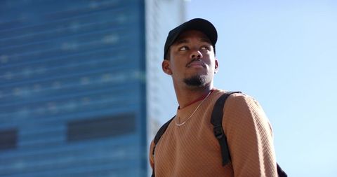 Young african american commuter looking up by glass tower urban backpacker portrait