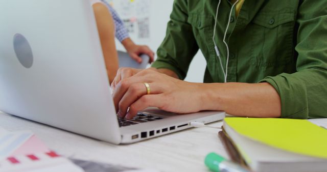 Hands typing on a laptop with headphones in a casual setting. Suitable for illustrating concepts like remote work, studying, freelancing, home office environment, multitasking, and focused productivity.