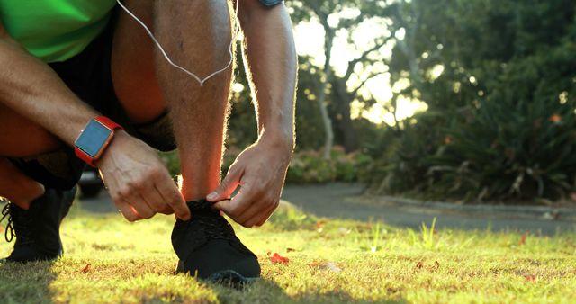 Man tying his shoe laces while jogging in park on a sunny day