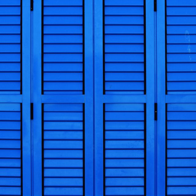 Blue wooden shutters with a repeating geometric pattern, creating a symmetrical design. Ideal for use in publications related to home decor, exterior design, and architecture. This vibrant photo can also be used as a background, texture, or within advertising campaigns focused on color and aesthetics.