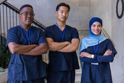 Diverse healthcare team standing arms crossed on clinic stairs wearing navy scrubs