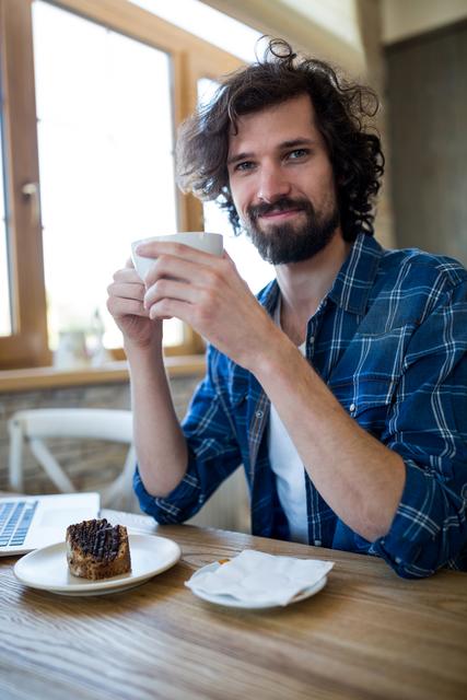Portrait of smiling man having coffee and pastry in coffee shop