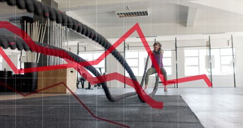 Woman exercising with battle ropes and graph overlay in gym