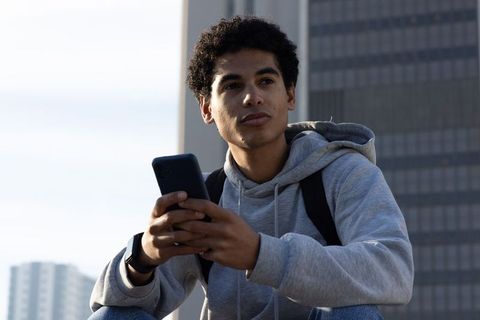 Contemplative african american teen holding smartphone on urban rooftop in hoodie