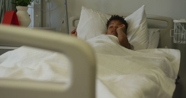 Child resting comfortably in a hospital bed, covered with white sheets. Ideal for use in healthcare and medical settings promotional material, health and wellness articles, hospital website designs, or informative blogs about pediatric care and recovery.