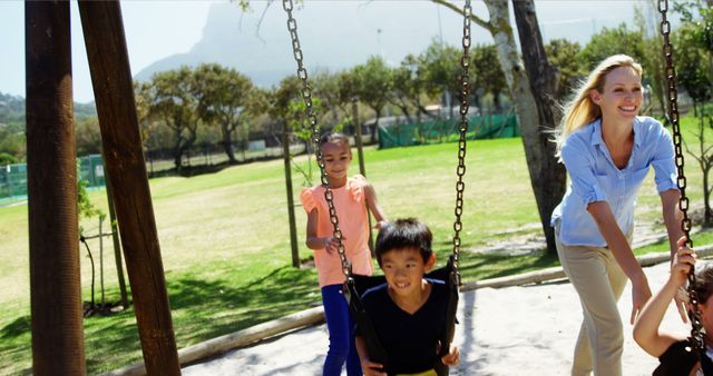 Happy trainer pushing schoolkids on swing in playground of school