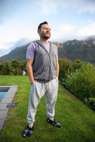 Mature asian man standing poolside on lawn wearing hoodie vest, sweatpants and plaid slippers