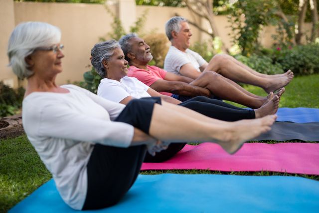 Dedicated senior friends doing stretching exercise while sitting on mats at park