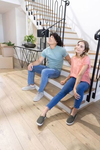 Young couple sitting on stairs unpacking moving boxes in modern minimalist home