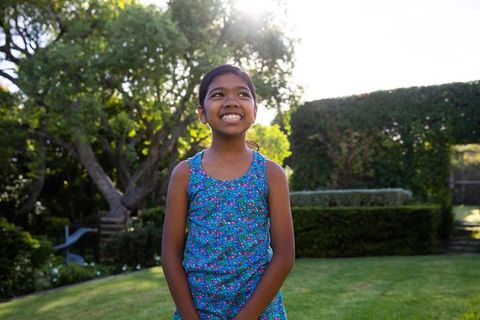 Cheerful Girl in Floral Dress Enjoying Sunlit Backyard