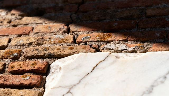 Diagonal fissure between white marble slab and aged terracotta brick with lichen patina