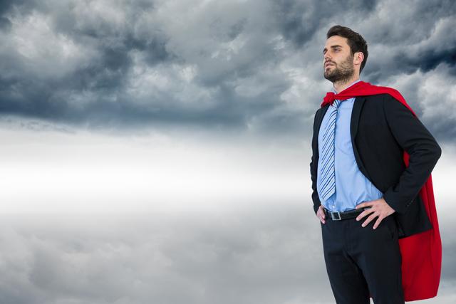 Businessman wearing a superhero cape stands confidently with hands on hips against dramatic cloudy sky. Represents leadership, determination, and success. Suitable for promoting corporate events, leadership seminars, motivational content, and success stories.