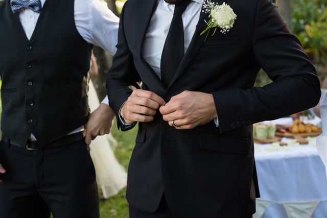 Groom buttoning his wedding suit outdoors, preparing for the ceremony. Ideal for wedding planning, bridal magazines, and event coordination materials. Highlights elegance and attention to detail in wedding attire.