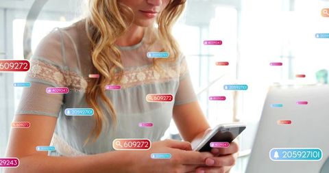 Young woman scrolling smartphone while working on laptop with floating social notifications