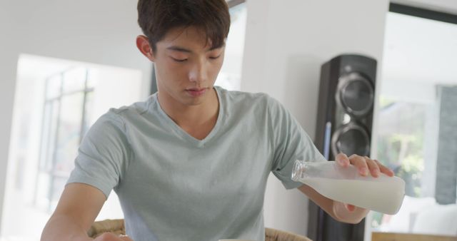 Asian boy pouring milk in his cereal bowl at home. teenager lifestyle and living concept