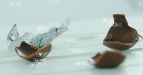 Close-up broken chocolate egg with foil wrapper and social media overlay on white wood