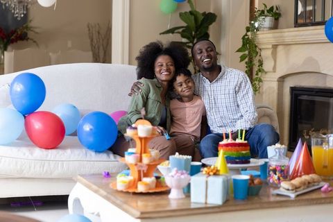Joyful family celebrating child's birthday at home with rainbow cake and colorful balloons
