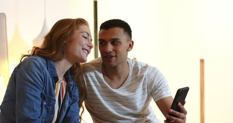 Happy couple video chatting with friends on smartphone in cozy room