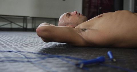Male Athlete Resting Shirtless on Rubber Gym Floor Sweating After HIIT Jump Rope Workout