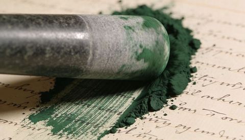 Art brayer rolling emerald pigment powder across vintage cursive paper for printmaking