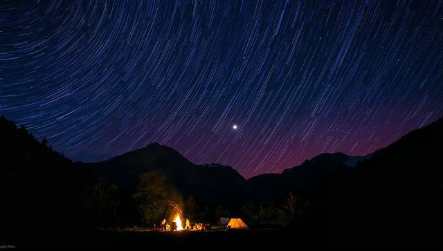 Campfire gathering under sweeping star trails over mountain valley long exposure nightscape