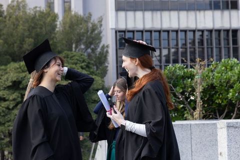 Graduating women celebrating together on campus with caps and diplomas