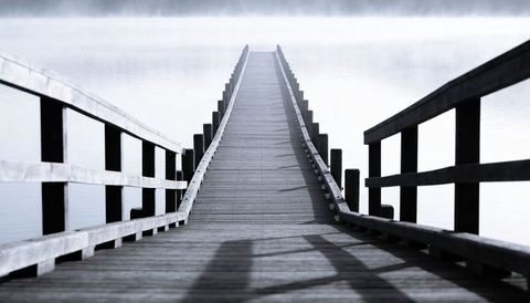 Misty wooden pier leading into fog over calm lake, minimalist moody boardwalk perspective