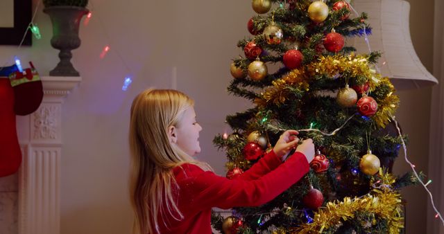 Child decorating a Christmas tree with colorful ornaments and tinsel indoor. Ideal for holiday greeting cards, family holiday promotions, festive advertising campaigns, or articles about Christmas traditions and family activities.