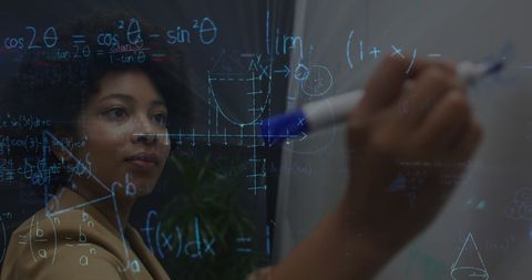Focused Businesswoman Writing Complex Equations on Transparent Board