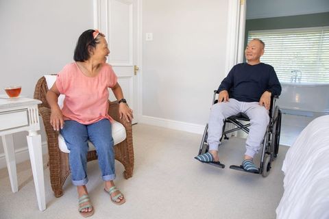 Senior asian couple sharing warm conversation in bedroom, woman sitting, man in wheelchair