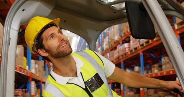 Smiling warehouse worker in a high-visibility vest and hard hat operating a forklift inside a large storage facility. Ideal for illustrating topics related to logistics, transportation, warehouse operations, inventory management, and workplace safety.