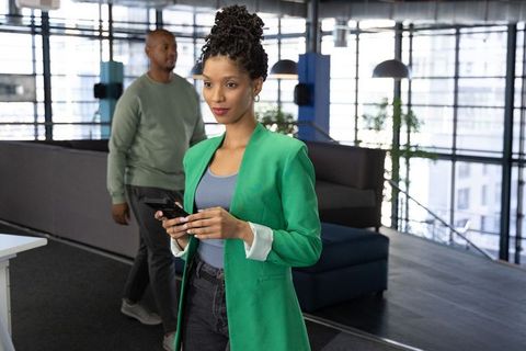 Confident african american woman holding phone in modern open-plan office lounge