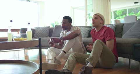 Multicultural friends playing video games on living room floor, modern bright interior