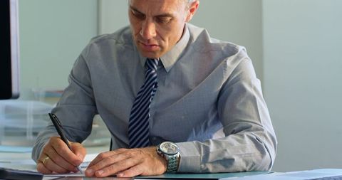 Mature Businessman Writing Notes at Office Desk