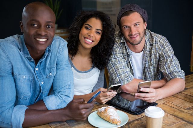 Portrait of smiling young friends holding smart phones at table in coffee shop